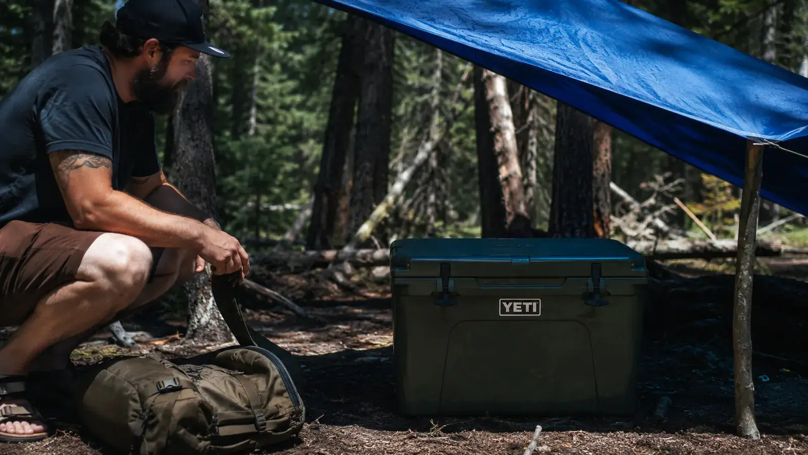 A camping cooler positioned in the shade under a camp tarp, away from direct sun, with a thermometer showing cool temperature