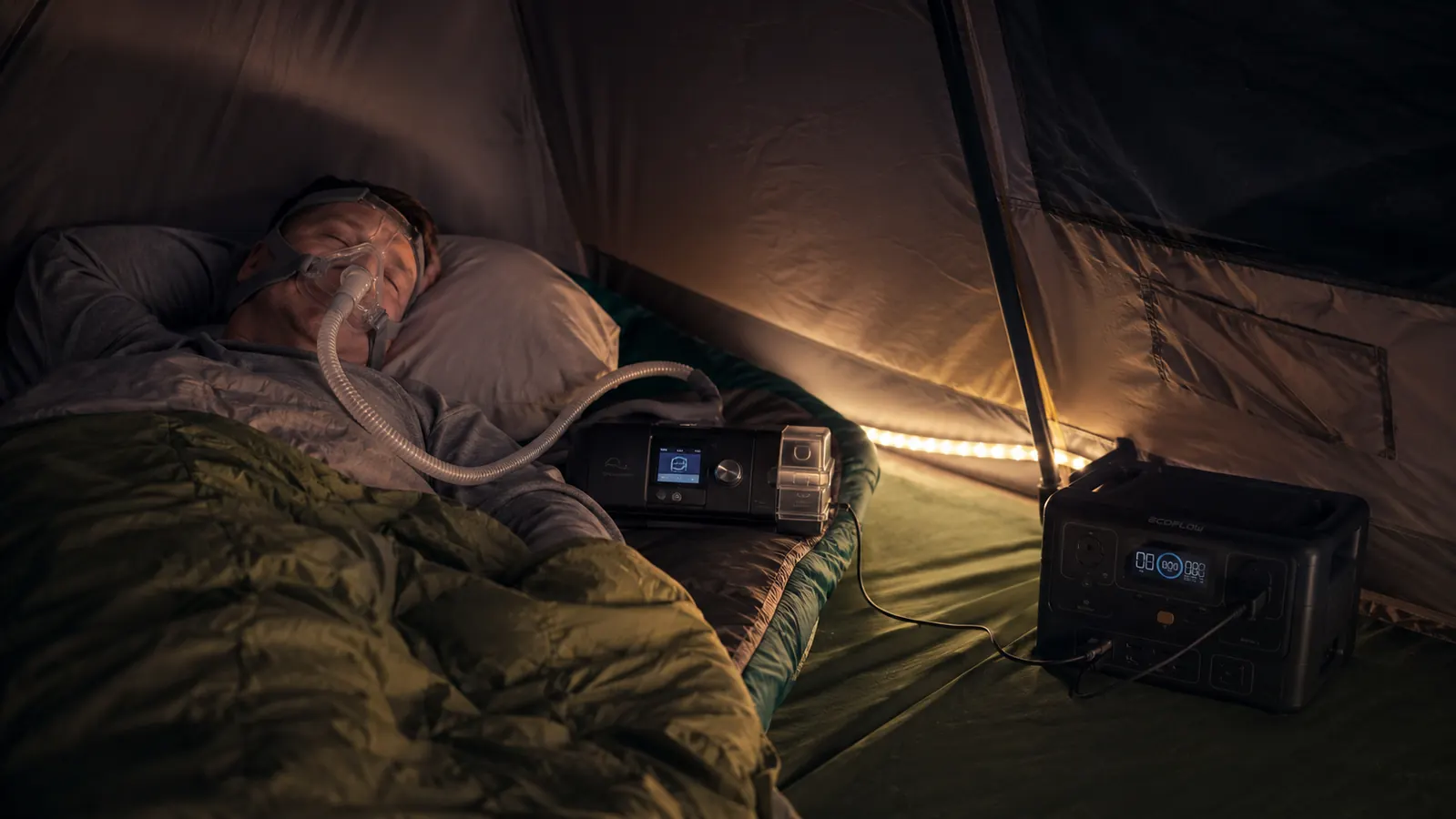 Camper using a CPAP machine powered by a portable power station inside a tent at night