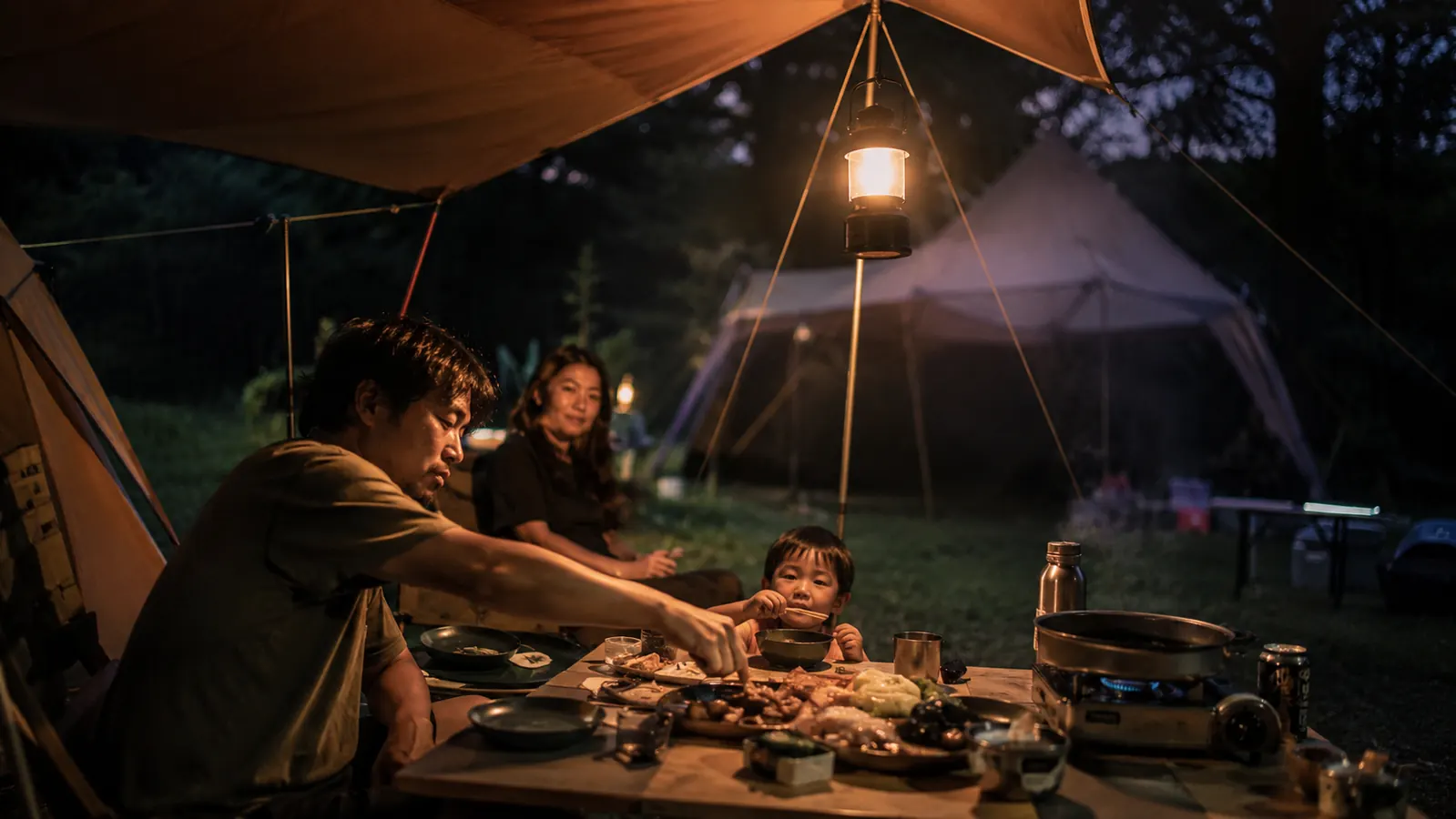 Lepro camping lantern hanging from a tent loop above a camp table set with dinner supplies