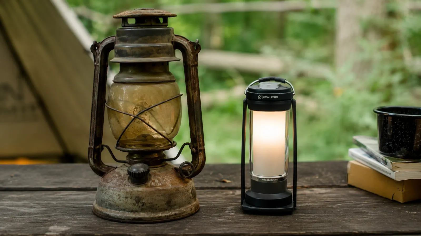 Old rusty propane gas lantern sitting beside a modern rechargeable LED lantern on a wooden camp table, dramatic contrast in size and condition