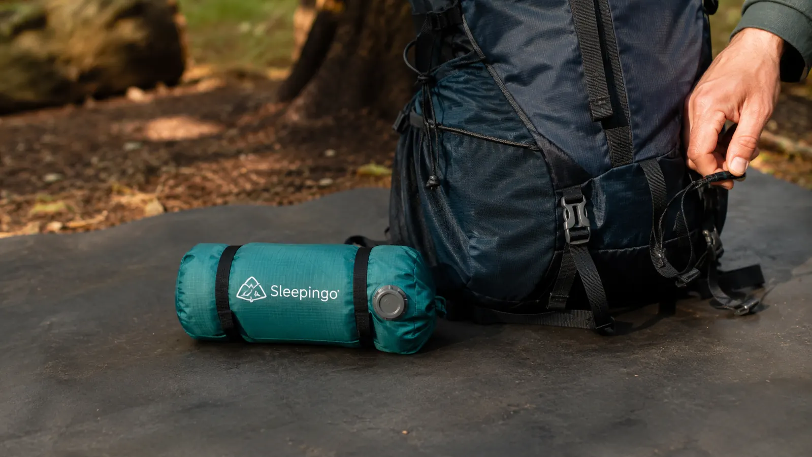 A rolled-up Sleepingo sleeping pad next to a small hiking pack to show compact size