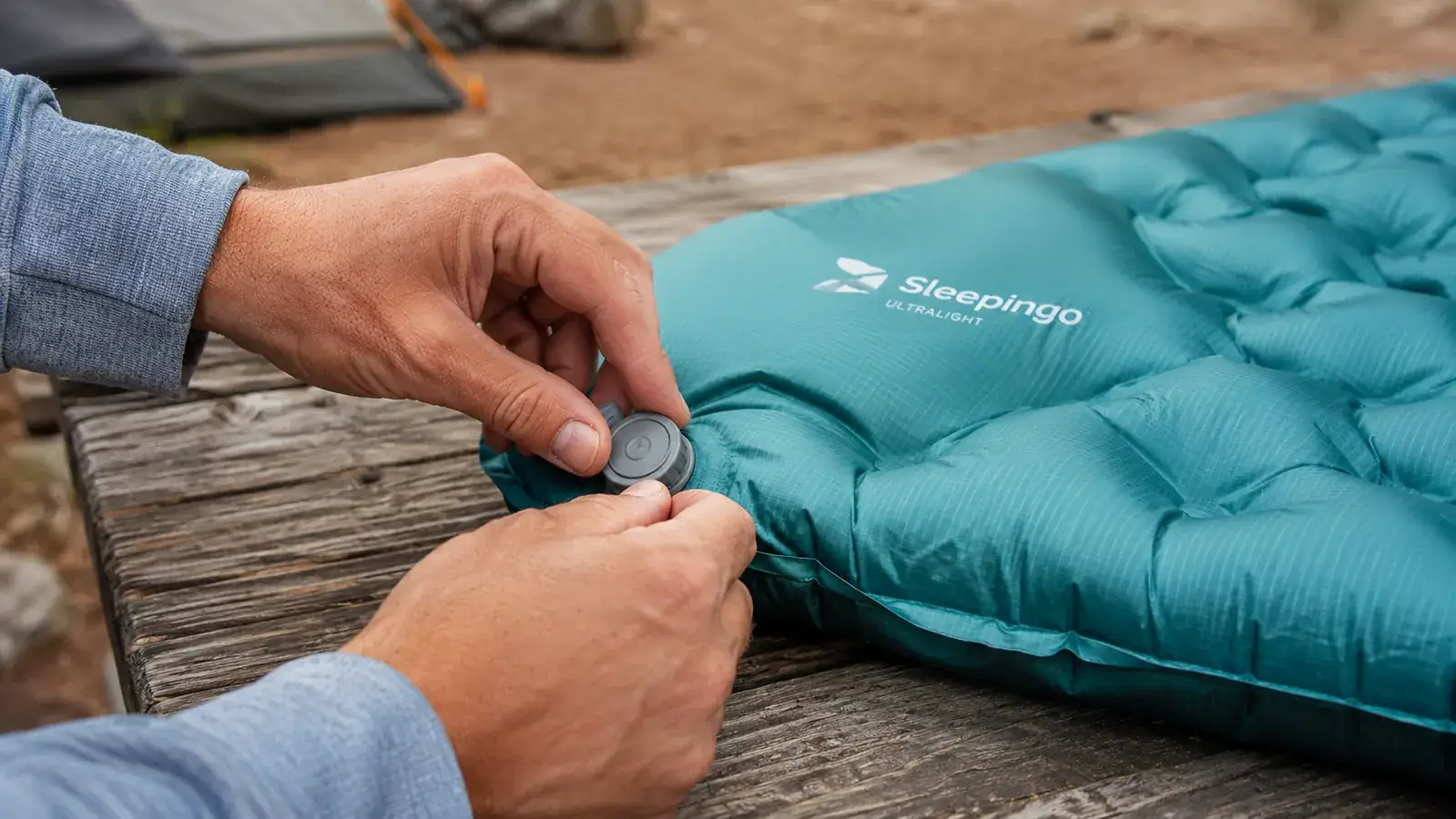 Hands opening the twist valve on the Sleepingo sleeping pad outdoors on a picnic table